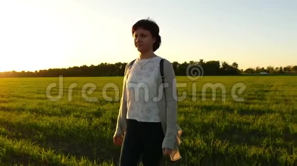 一个年轻的女人在夕阳的背景下沿着绿色的草坪缓慢地走着视频的预览图