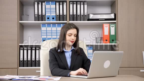 女商人在办公桌前用手提电脑打字然后微笑着对着镜头视频的预览图