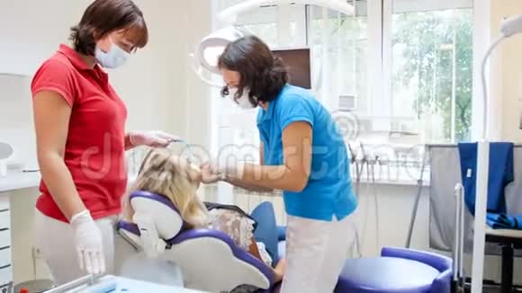 牙科医生与护士治疗坐在牙科椅上的年轻女子的4k录像视频的预览图