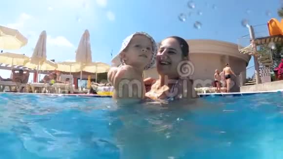 在水上公园游泳池里带着年轻母亲微笑的幼儿男孩慢镜头视频的预览图