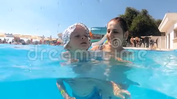 慢动作视频快乐微笑的年轻女子与她蹒跚学步的儿子在游泳池在酒店度假村视频的预览图