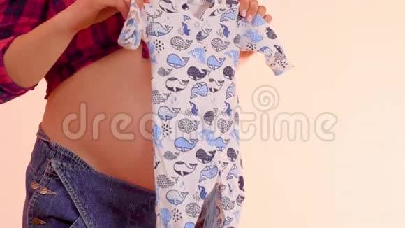 孕妇手里拿着滑块在她赤裸的大肚子上怀着可爱婴儿衣服的孕妇视频的预览图