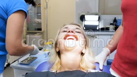 牙科诊所牙科椅上有口宽器的女性病人的4k镜头视频的预览图