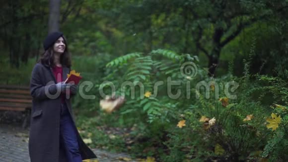 快乐的黑发女人带着一本书微笑着走在树叶下视频的预览图