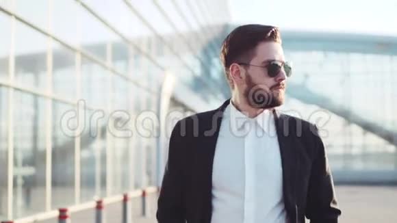 英俊的胡子男戴着太阳镜走在机场航站楼附近接电话节点时尚优雅视频的预览图