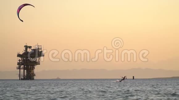女人在海上玩风筝在水面上滑翔在背景上钻油机视频的预览图