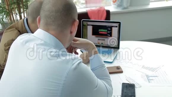 两个商人坐在笔记本电脑旁监控业务的发展商务视频的预览图