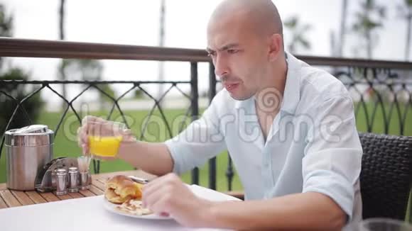 一个穿着蓝色衬衫的年轻人正在街上的咖啡馆里吃早餐视频的预览图