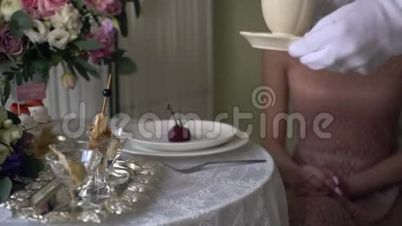 戴着白手套的侍者在女孩面前的桌子上放了一杯茶视频的预览图
