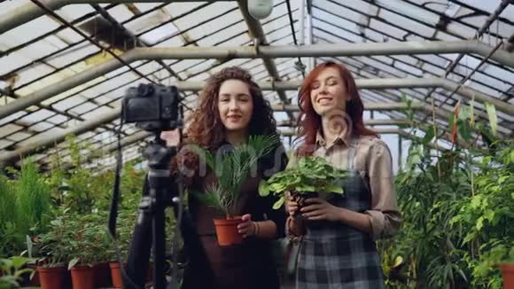 穿着围裙微笑的年轻女性园丁正拿着鲜花在网上为vlog录制视频博客视频的预览图