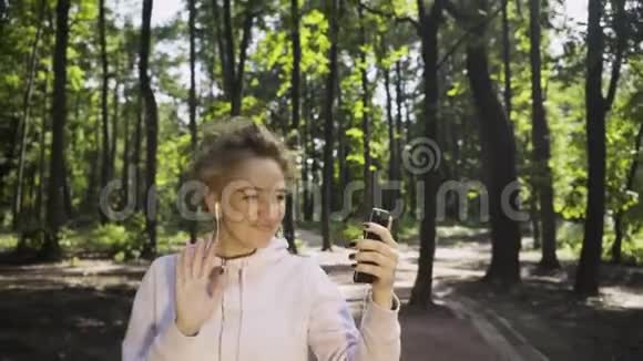 年轻女子在公园慢跑和视频聊天视频的预览图