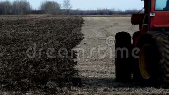 红农场拖拉机拉耕机在收获大豆后在田间翻耕黑土视频的预览图