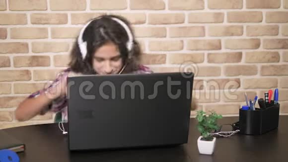 酷酷的少年男孩一头卷曲的黑发穿着格子衬衫戴着耳机跳舞坐在笔记本电脑前视频的预览图