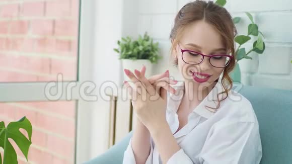在舒适的客厅里照顾年轻女性的身体坐在椅子上的漂亮女孩把奶油涂在她的手皮上视频的预览图