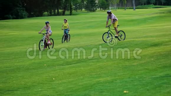 四个快乐的学生在绿色的草坪上骑自行车视频的预览图