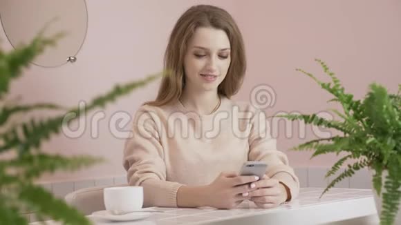 女人在咖啡馆里使用智能手机喝着咖啡微笑着在手机互联网上发短信交流和视频的预览图