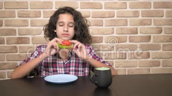 有胃口的饥饿少年在阁楼式的厨房里吃一个三明治里面有新鲜的生菜和西红柿视频的预览图