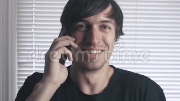 幸福的年轻人在电话里说话在百叶窗的背景下微笑的画像视频的预览图