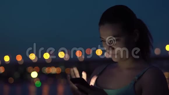 一个女孩晚上在城市的背景下使用一部手机视频的预览图