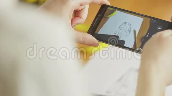 时装设计师在工作室的智能手机上拍摄服装草图的特写镜头视频的预览图