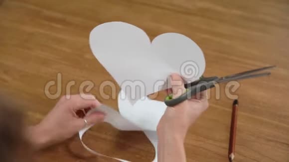一个年轻的女人在白纸上画一颗心然后用剪刀把它剪下来为爱制作礼物视频的预览图