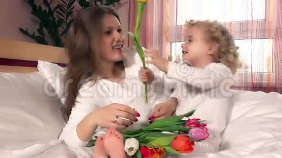 可爱的妈妈和小女孩家里的床上放着一束郁金香花视频的预览图