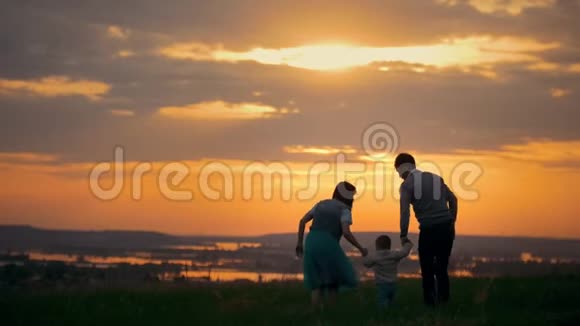 快乐的传统家庭步行户外妈妈爸爸和小儿子在夏季草地日落视频的预览图