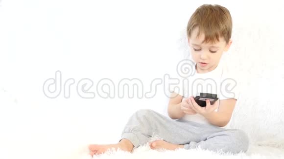 快乐的孩子在白色背景下玩着智能手机微笑着运动摄像机滑块视频的预览图