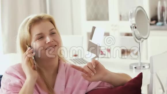 一位穿着家庭浴袍坐在客厅沙发上打电话的年轻女子视频的预览图