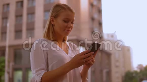 金发女性在户外滚动触摸屏手机视频的预览图