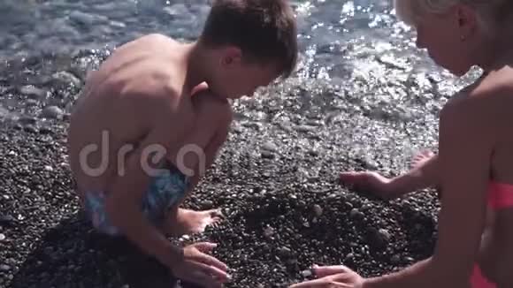 年轻苗条的母亲和儿子在沙滩上玩石子动作缓慢视频的预览图