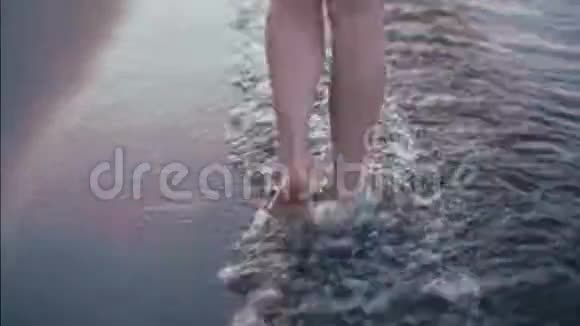 手持特写镜头在海浪中赤脚沿着海岸行走的女士腿视频的预览图