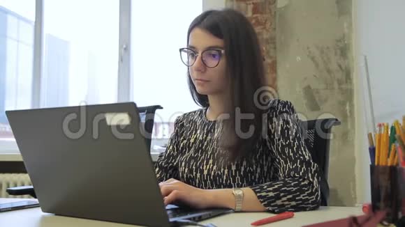 年轻的黑发正在工作坐在办公桌前笔记本电脑在现代办公室视频的预览图