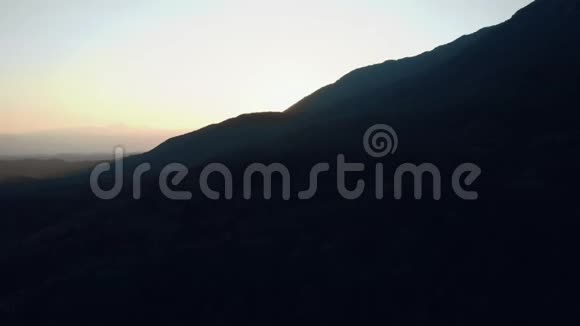 从空中俯瞰一座覆盖着森林的黑暗山丘朝日出日落方向前进视频的预览图