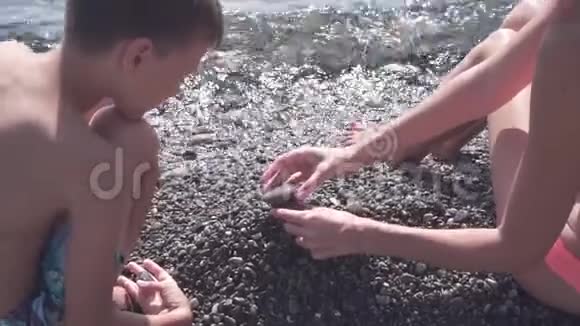 年轻苗条的母亲和儿子在沙滩上玩石子动作缓慢视频的预览图