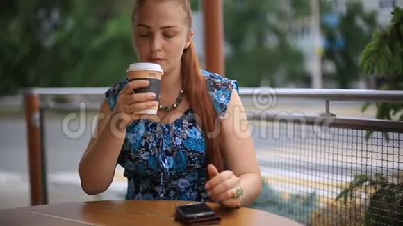 一个红头发的漂亮女人坐在街头咖啡馆的桌子旁喝咖啡视频的预览图