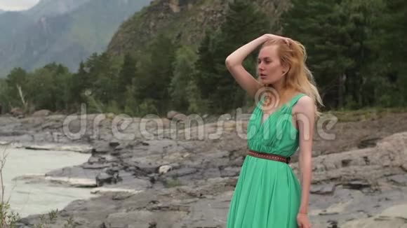 年轻的女人穿着一件长长的流动的衣服在河山的背景上穿绿色衣服的女人视频的预览图