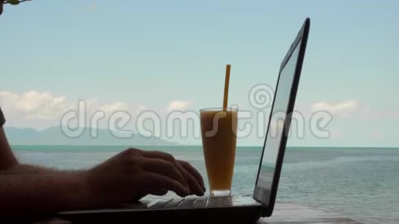 年轻的高加索人使用笔记本电脑和饮用芒果水果奶昔与海景远程工作和自由职业概念男性视频的预览图