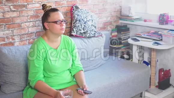 年轻无聊的女人坐在家里的沙发上看电视4k视频的预览图