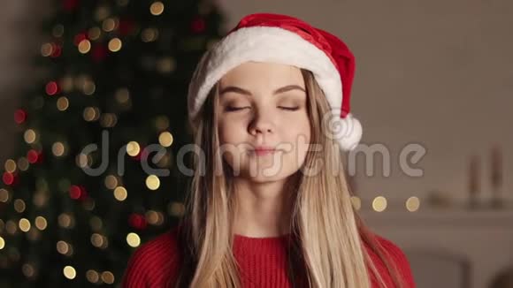 快乐无忧无虑的金发女人在圣诞灯光的背景下亲吻一个戴着圣诞帽的漂亮女孩视频的预览图