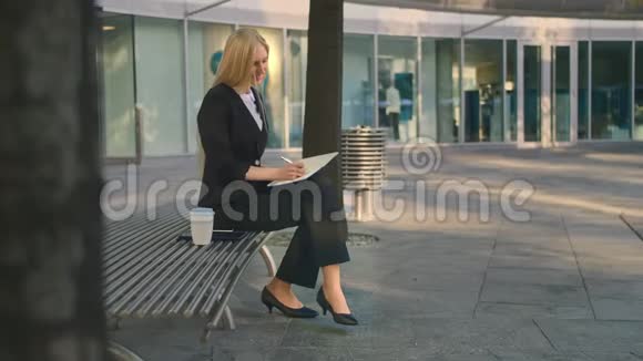 成功的商业女性在户外做笔记在露台和露台上坐在长凳上的优雅女商人的侧景视频的预览图