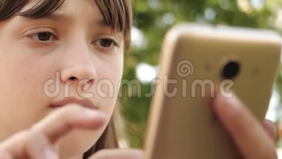 快乐女孩用智能手机在长凳上的公园里翻页特写镜头年轻的千禧年视频的预览图