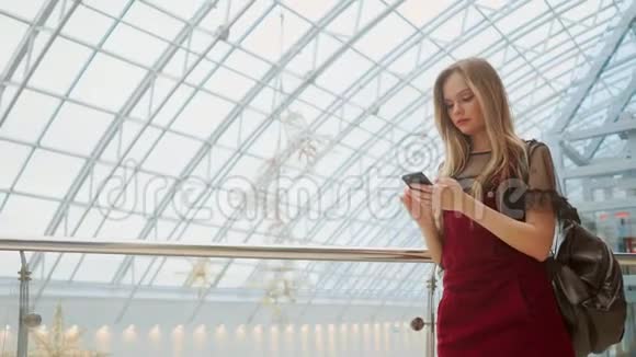 年轻的女游客戴着帽子背包站在机场使用智能手机偷鸡摸狗的女孩检查电子邮件聊天视频的预览图