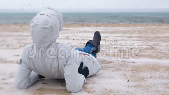 冬天女游客躺在海边一片雪白的沙滩上穿夹克和牛仔裤的女人后视图视频的预览图