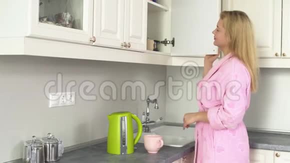 一位穿着家庭浴袍的年轻女士拿着一个带茶的罐子享受它的气味视频的预览图
