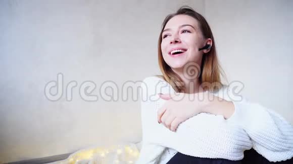 可爱的女孩的肖像通过蓝牙耳机与微笑聊天坐在地板上的格子在明亮的房间与视频的预览图