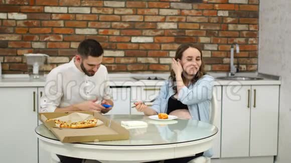 男人和孕妇在家里厨房里吃披萨吃饭的时候有人打电话视频的预览图