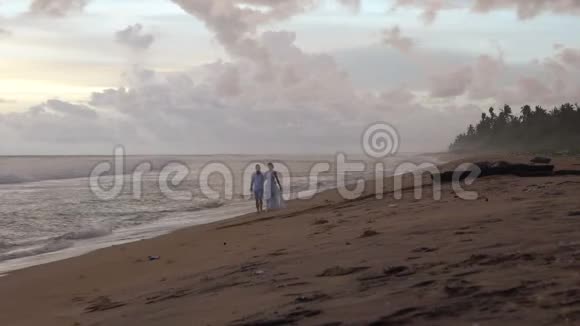 恋爱中的年轻夫妇在日落时分在海滩上散步手牵手视频的预览图