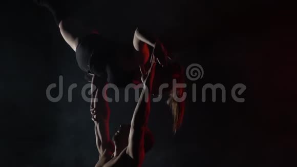 慢动作射击一个男人抱着一个女人在他的怀里在黑暗中做杂技瑜伽视频的预览图