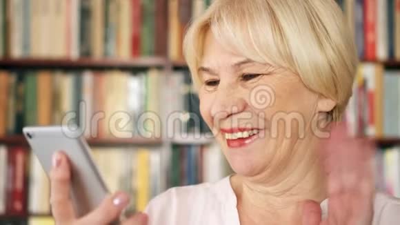 现代高级妇女在家里通过信使应用程序在图书馆交谈背景书架视频的预览图